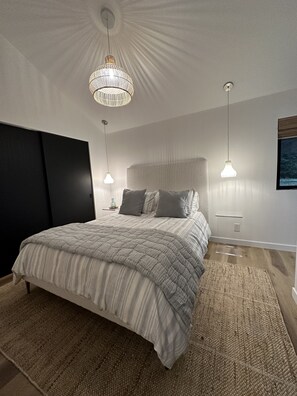 A modern bedroom with a large bed, two bedside tables, and a chandelier. - The Sprout  - gas fire-pit, grilling staton, hot tub, close to shops & hiking (Juneau)