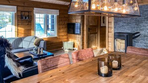 A cozy log cabin interior with a wooden dining table, cushioned seating, a fireplace, and a television mounted on the wall. - 3 bedroom lovely home in Bjorli (Bjorli)