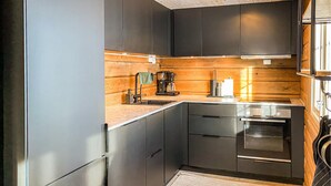 A modern kitchen with dark cabinetry, a wooden backsplash, a built-in oven, and a coffee maker. - 3 bedroom lovely home in Bjorli (Bjorli)