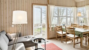 A cozy room with a sofa, a dining table with chairs, a lamp, and large windows with curtains.