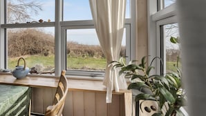 A cozy room with a wooden bench, a table with a teapot, and a view of a grassy field through large windows.