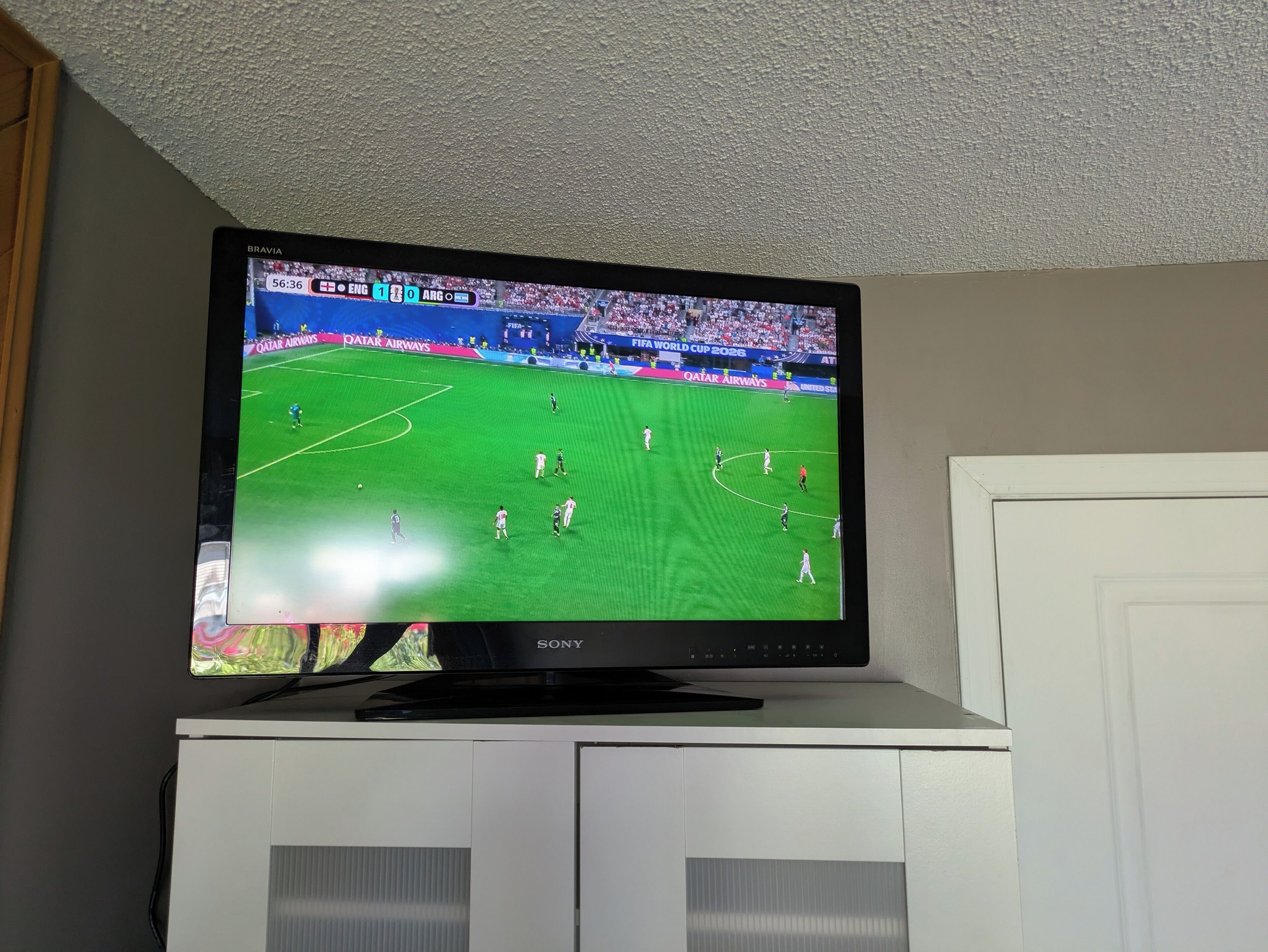 A flat-screen TV on a cabinet displaying a soccer match.