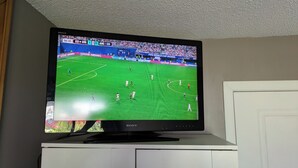 A flat-screen TV on a cabinet displaying a soccer match. - Quiet cozy room no stairs in a peaceful house, safe community, full kitchen (Langley Township)