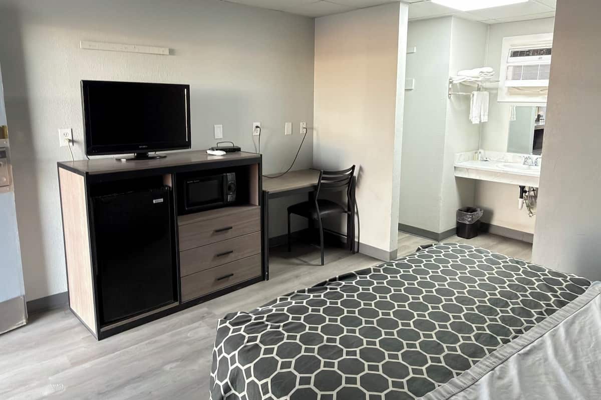 A hotel room with a bed, a desk, a television, a mini-fridge, and a bathroom.