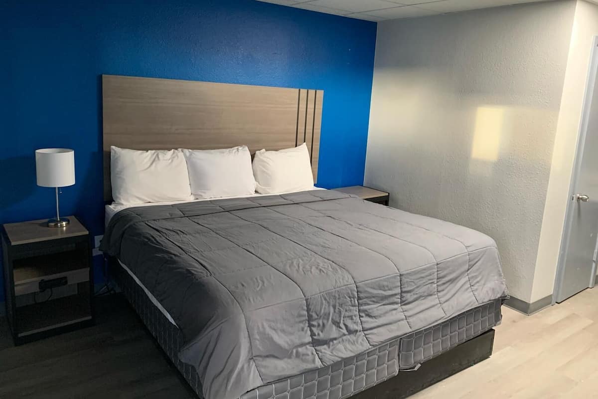 A hotel room with a bed, a nightstand, a lamp, and a door.