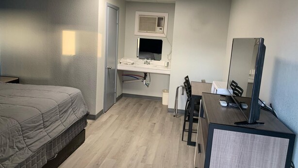 A hotel room with a bed, a desk with a computer, a mirror, a window, and a bathroom with a sink and toilet. - JAL COUNTRY INN (Jal)