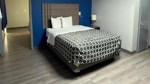 A hotel room with a bed, a nightstand, a lamp, a door, and a hallway. - JAL COUNTRY INN (Jal)