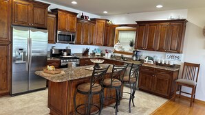 A modern kitchen with wooden cabinets, stainless steel appliances, and a central island with bar stools. - Cozy River View House (Nanjemoy)