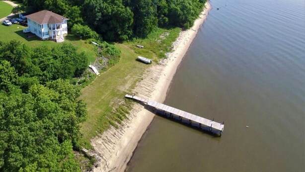 An aerial view of a house with a dock extending into a calm body of water, surrounded by dense greenery. - Cozy River View House (Nanjemoy)