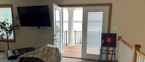 Ein Wohnzimmer mit einem dunkelbraunen Ledersofa, einem Flachbildfernseher, einem großen Fenster mit Jalousien und Blick auf einen Balkon.