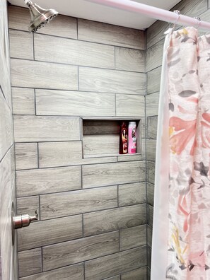 Ein Badezimmer mit Duschbereich, das durch eine Holzvertäfelung und einem kleinen Ablagebereich für Toilettenartikel gekennzeichnet ist.