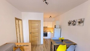 Un espace de vie compact comprenant un coin cuisine, un coin repas avec une table et des chaises, et un canapé avec des coussins.