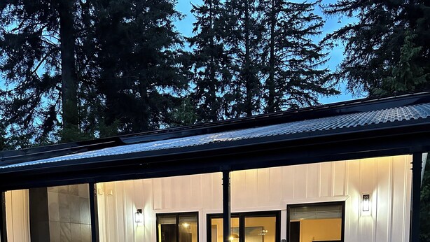 Ein modernes Haus mit überdachter Terrasse, großen Fenstern und einem Kamin.