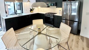 Eine moderne Küche mit Esstisch aus Glas, Korbstühlen, einem Edelstahlkühlschrank und einem eingebauten Backofen.