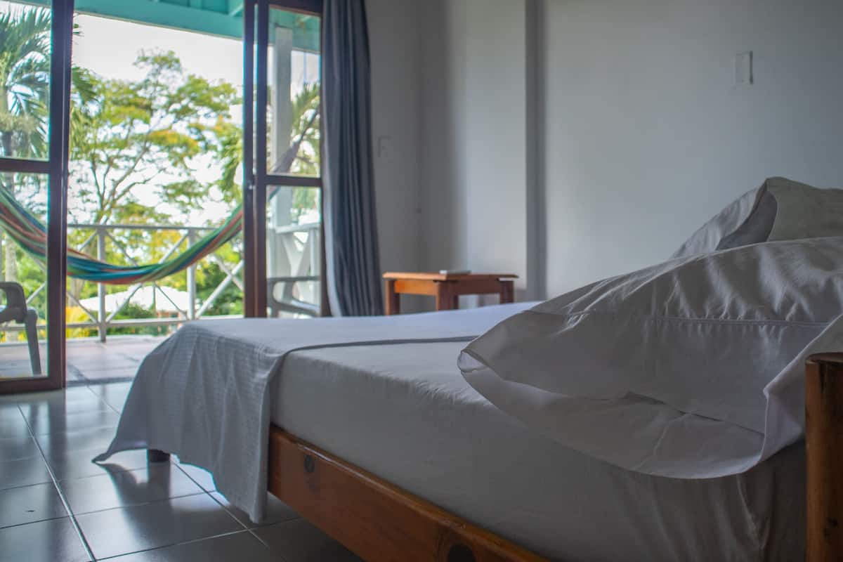 Une chambre avec un lit, une petite table et un hamac à l’extérieur de la fenêtre.