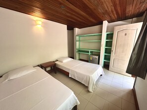 A room with two beds, a wooden ceiling, a wall-mounted light, and a green shelf unit.
