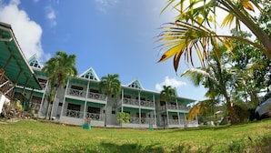 A two-story building with a green roof and white walls, surrounded by grass and palm trees. - South West Bay Cabañas (Providencia)