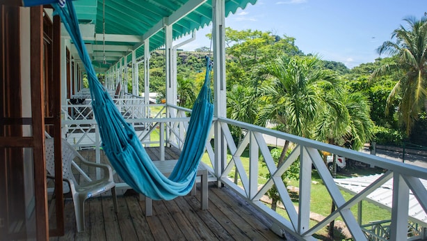 A wooden deck with a hammock, white railings, and a view of lush greenery and hills. - South West Bay Cabañas (Providencia)