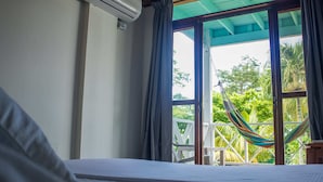 A room with a bed, an air conditioner, a window with curtains, and a hammock outside. - South West Bay Cabañas (Providencia)
