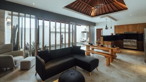 Una sala de estar moderna con un sofá modular, una mesa de comedor de madera y una cocina con encimera negra y electrodomésticos de acero inoxidable.