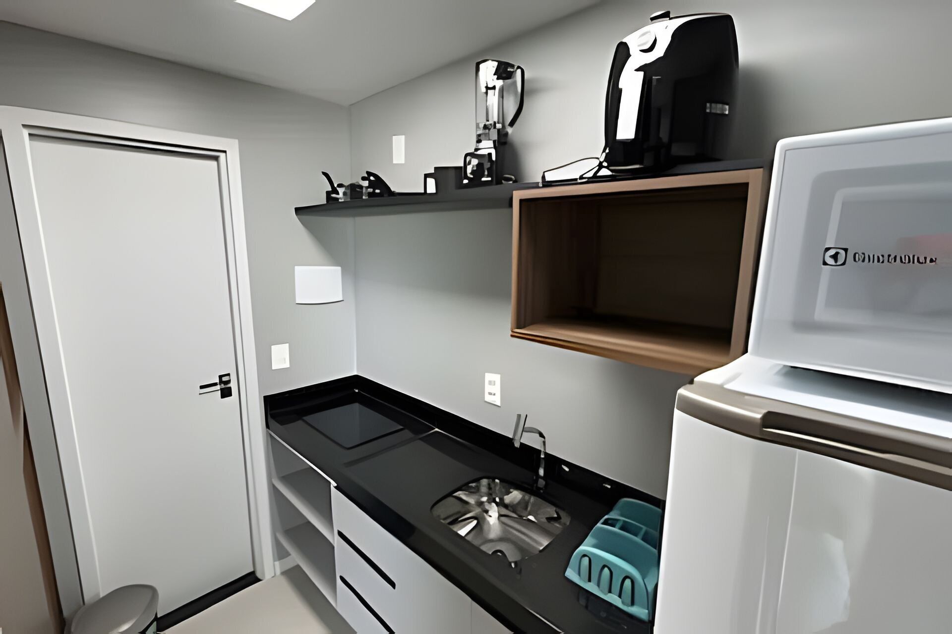 A compact kitchen with a black countertop, a sink, a coffee maker, and a refrigerator.