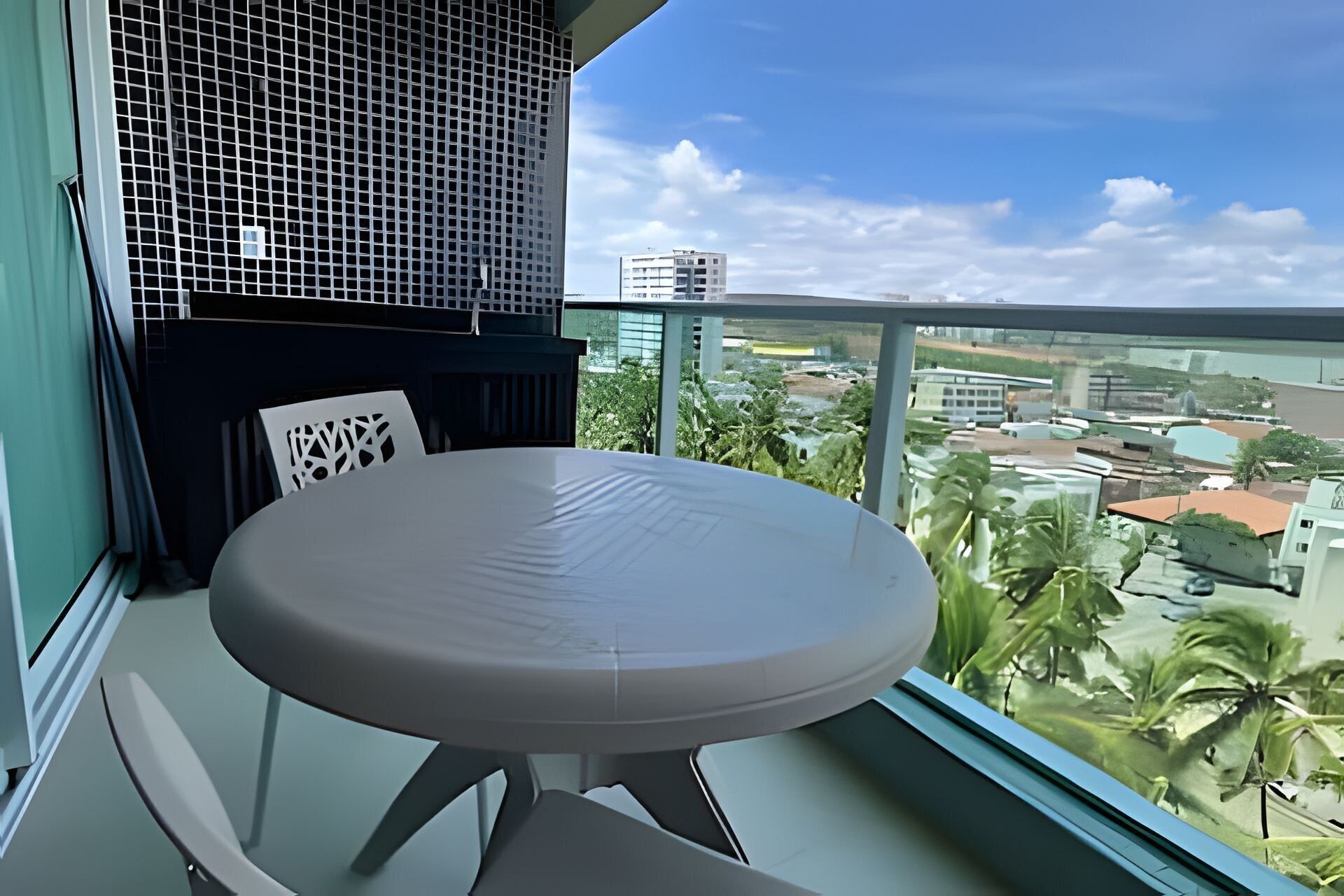 A balcony with a round table and chairs, a view of the cityscape, and a building with a grid-like facade.