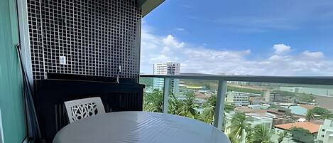 A balcony with a round table and chairs, a view of the cityscape, and a building with a grid-like facade.