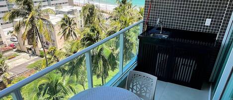 Un balcón con mesa y sillas, con vista a una playa y palmeras.