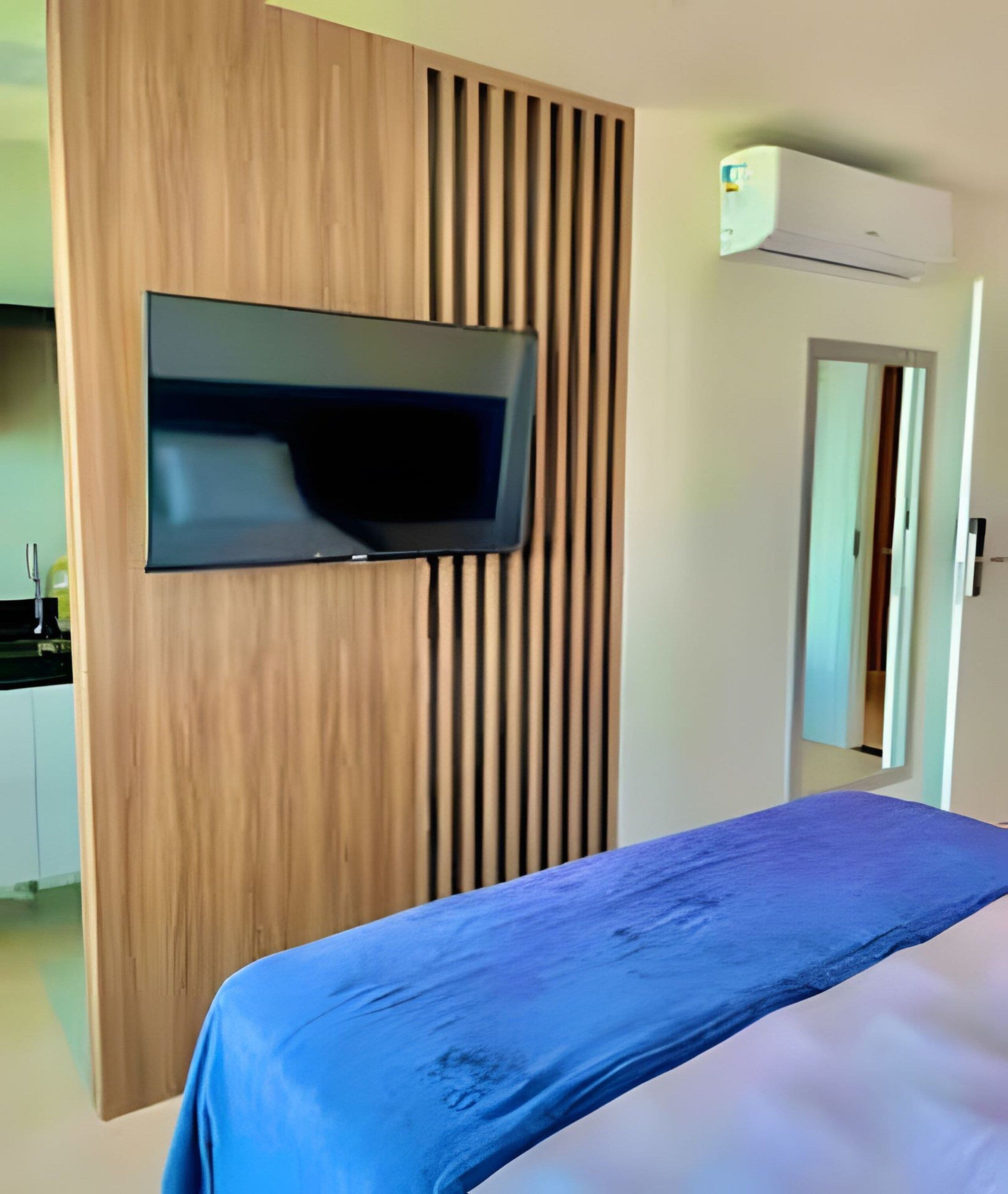 Una habitación de hotel con una cama, un televisor instalado en un panel de madera y un equipo de aire acondicionado en la pared.