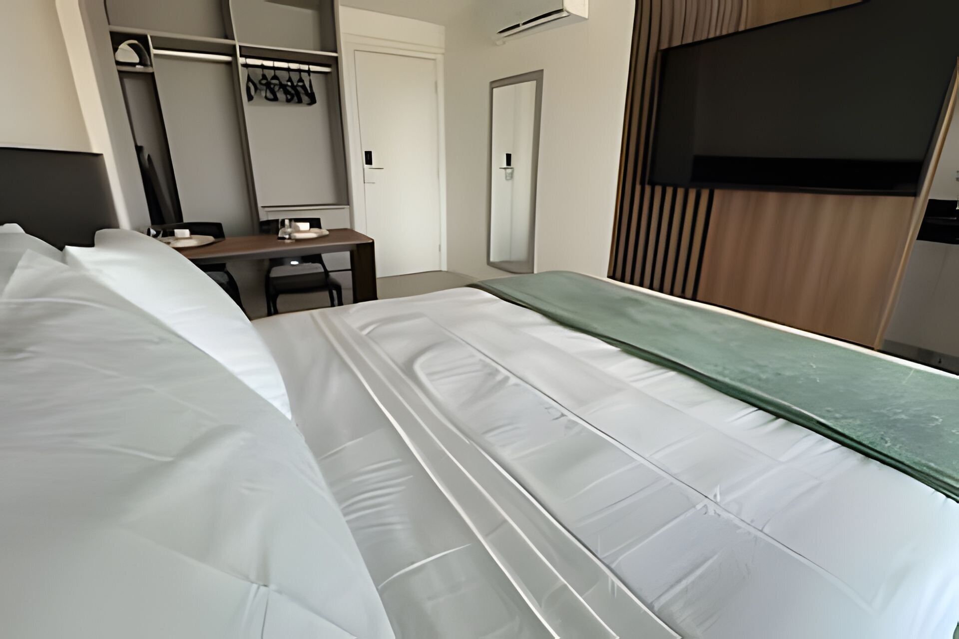 A hotel room with a bed, a desk, a chair, a wardrobe, and a television.