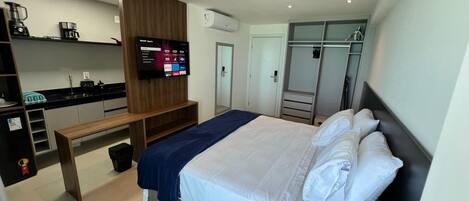 A hotel room with a bed, a TV, a wardrobe, a bench, and a kitchenette.