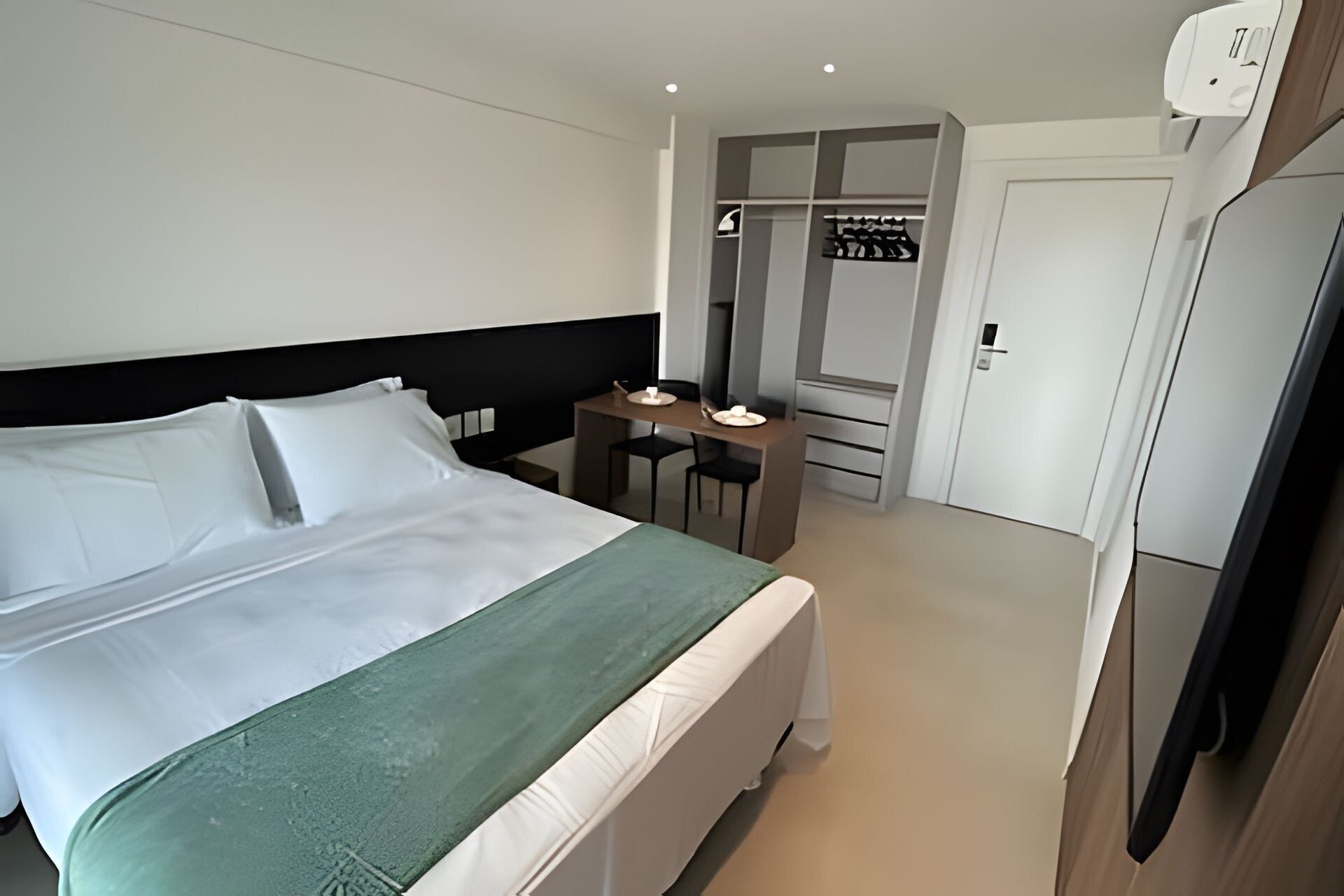 A hotel room with a bed, a desk, a wardrobe, and a door.