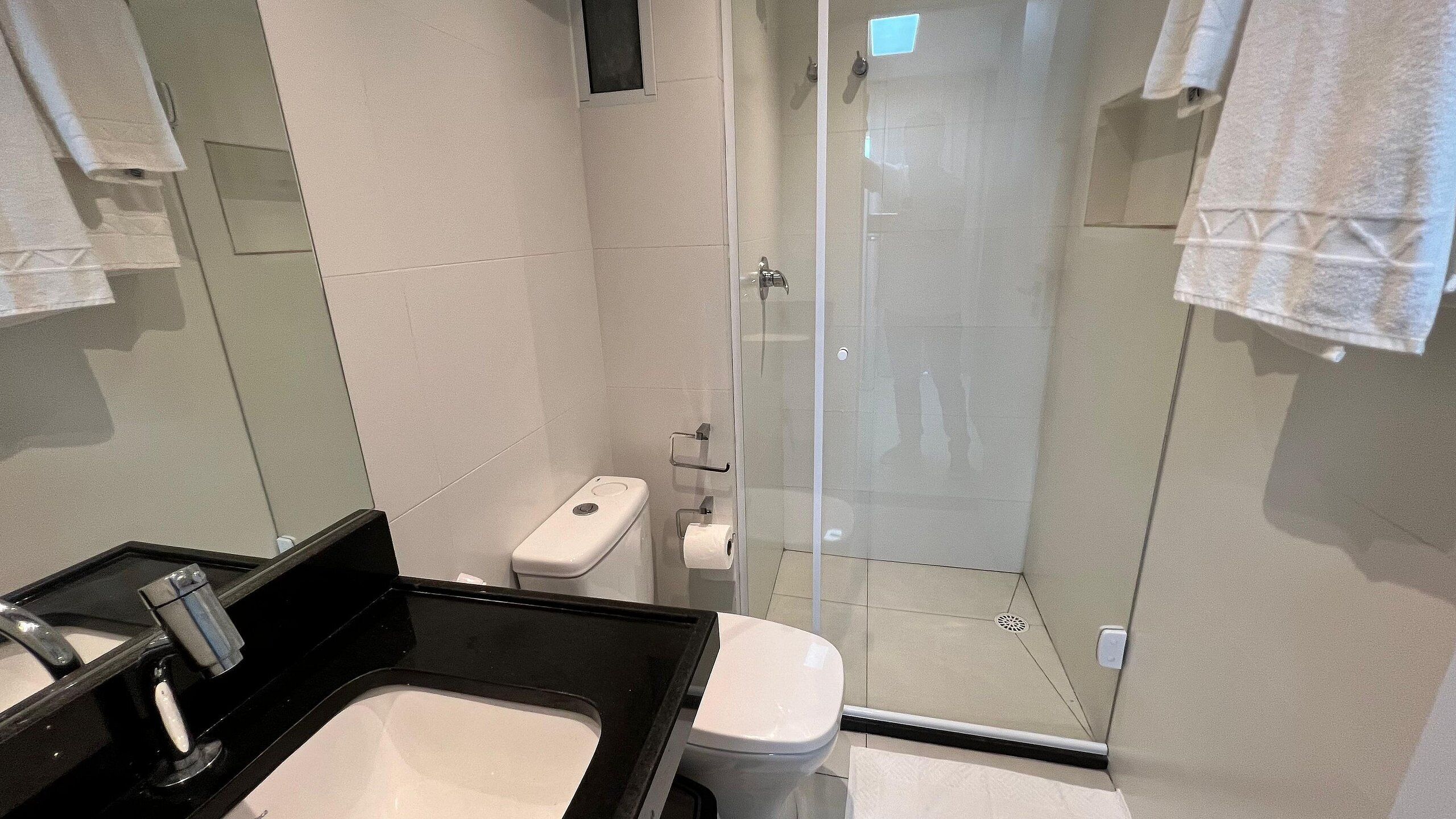 Een moderne badkamer met een douchecabine van glas, een zwart wastafelmeubel en een toilet.