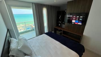 A hotel room with a bed, a TV, and a view of the ocean.