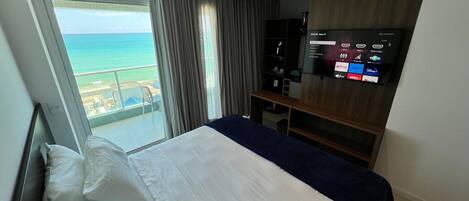 A hotel room with a bed, a TV, and a view of the ocean.