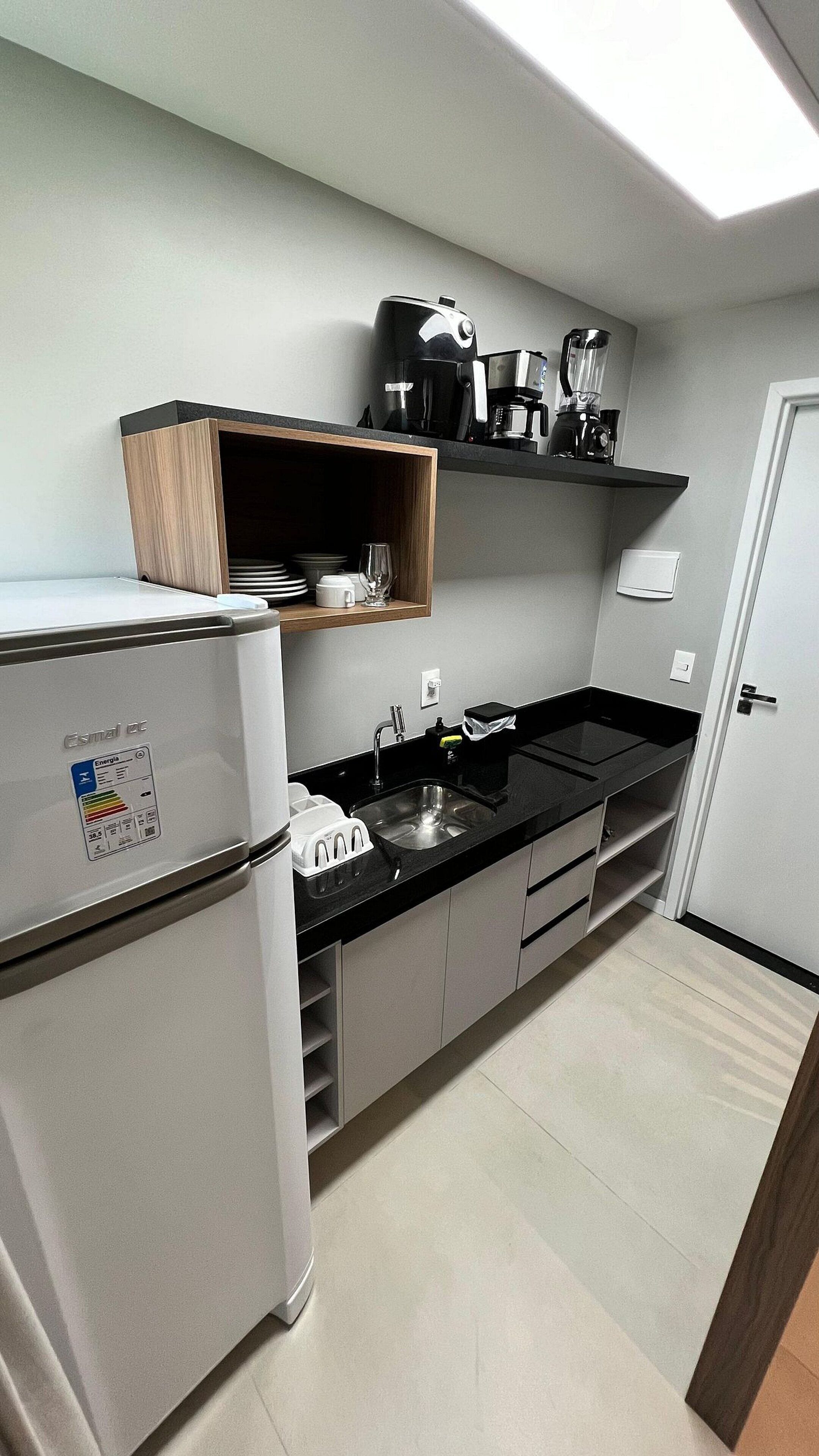 Eine kleine Küche mit einem Kühlschrank, einer Spüle und einer Kaffeemaschine auf einer schwarzen Arbeitsplatte.