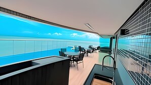 A modern interior with a long counter, black chairs, and a view of the ocean through a large window.