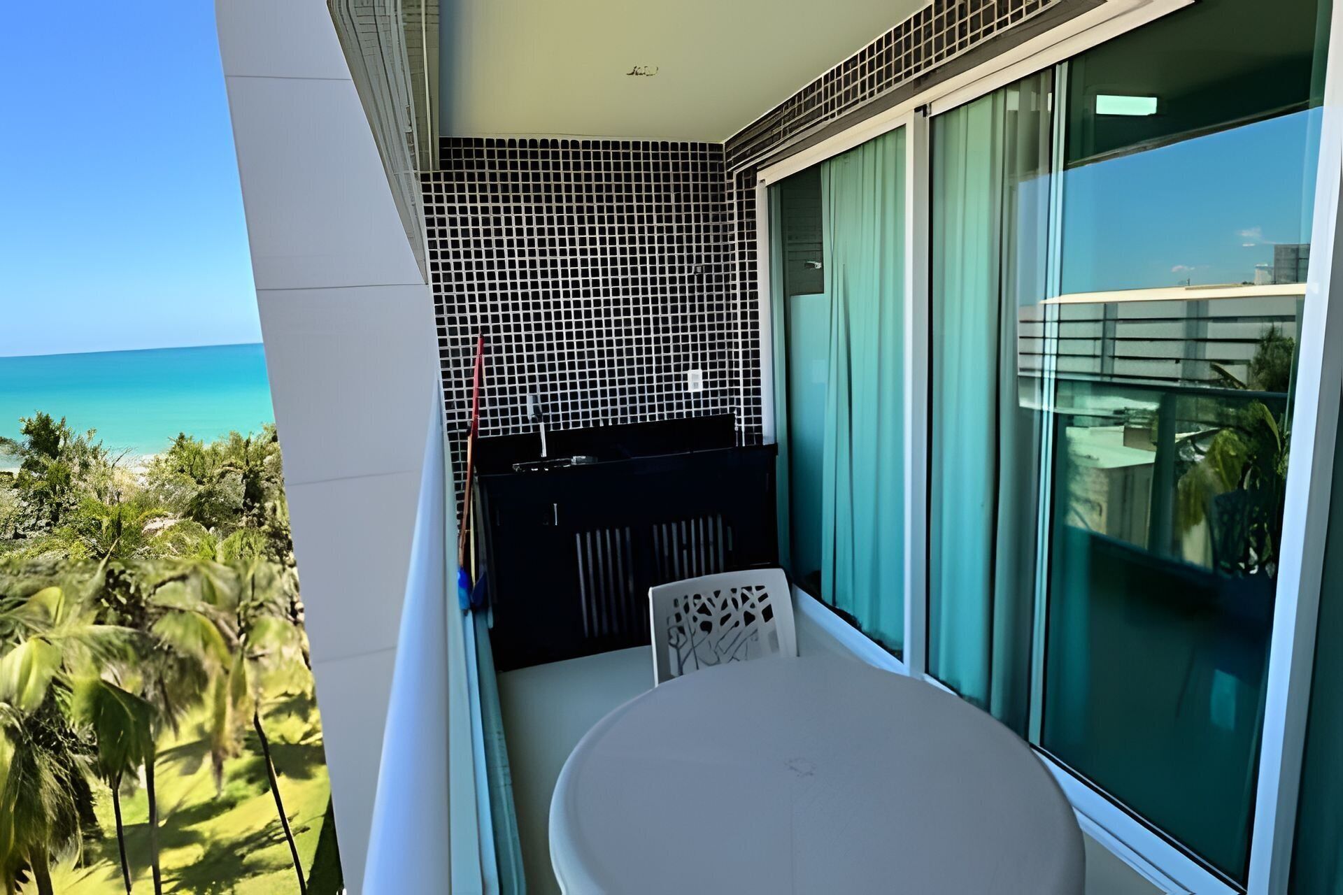 A balcony with a view of the ocean, a white table, and a chair.
