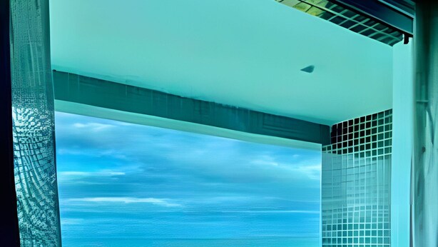 A balcony with a view of the ocean, a round table, and a small seating area.