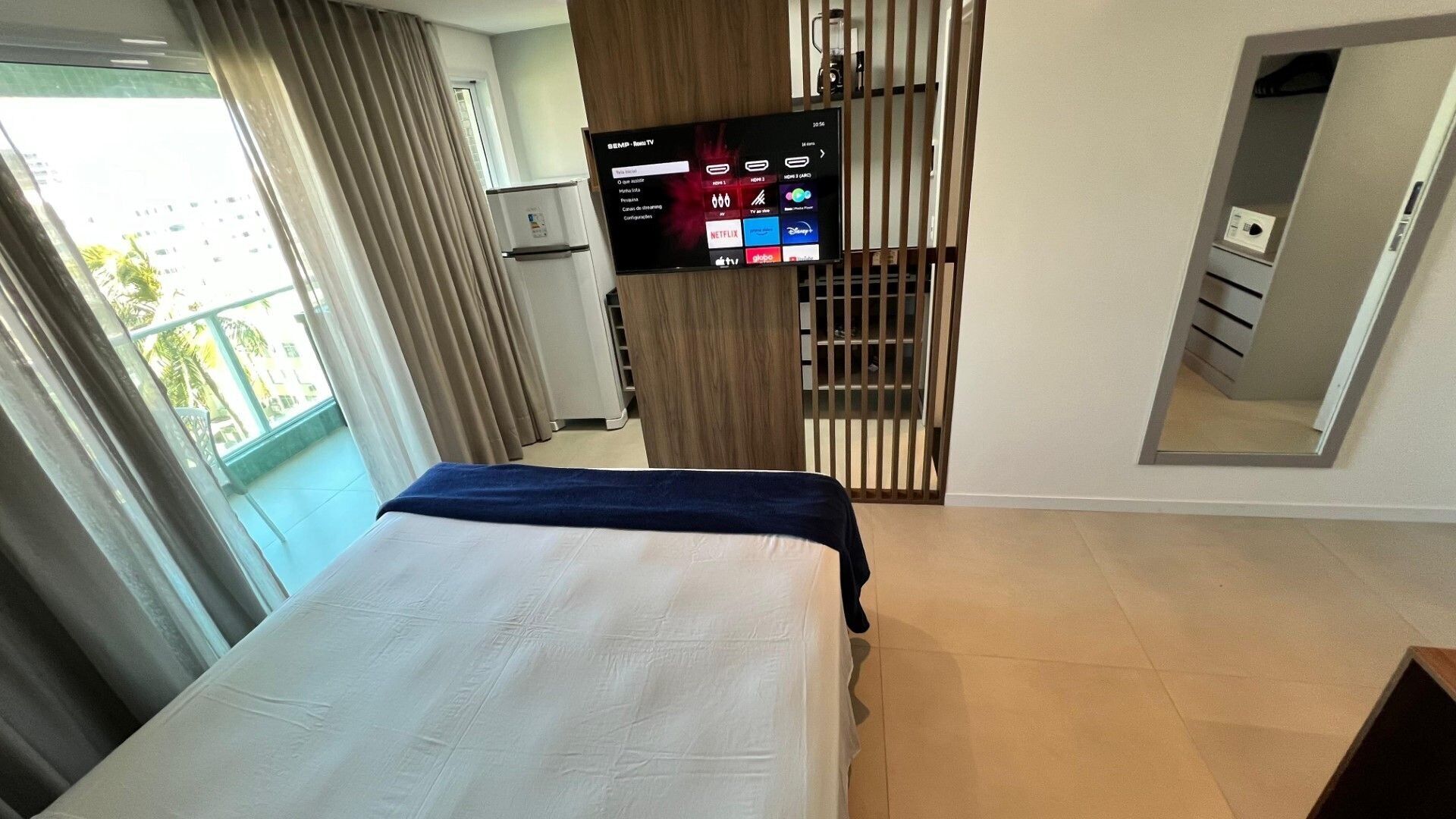 Une chambre d’hôtel avec un lit, un téléviseur fixé au mur, une porte coulissante et une vue sur l’extérieur.