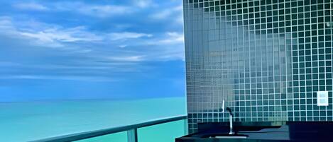 A balcony with a view of the ocean, a round table, and a chair.