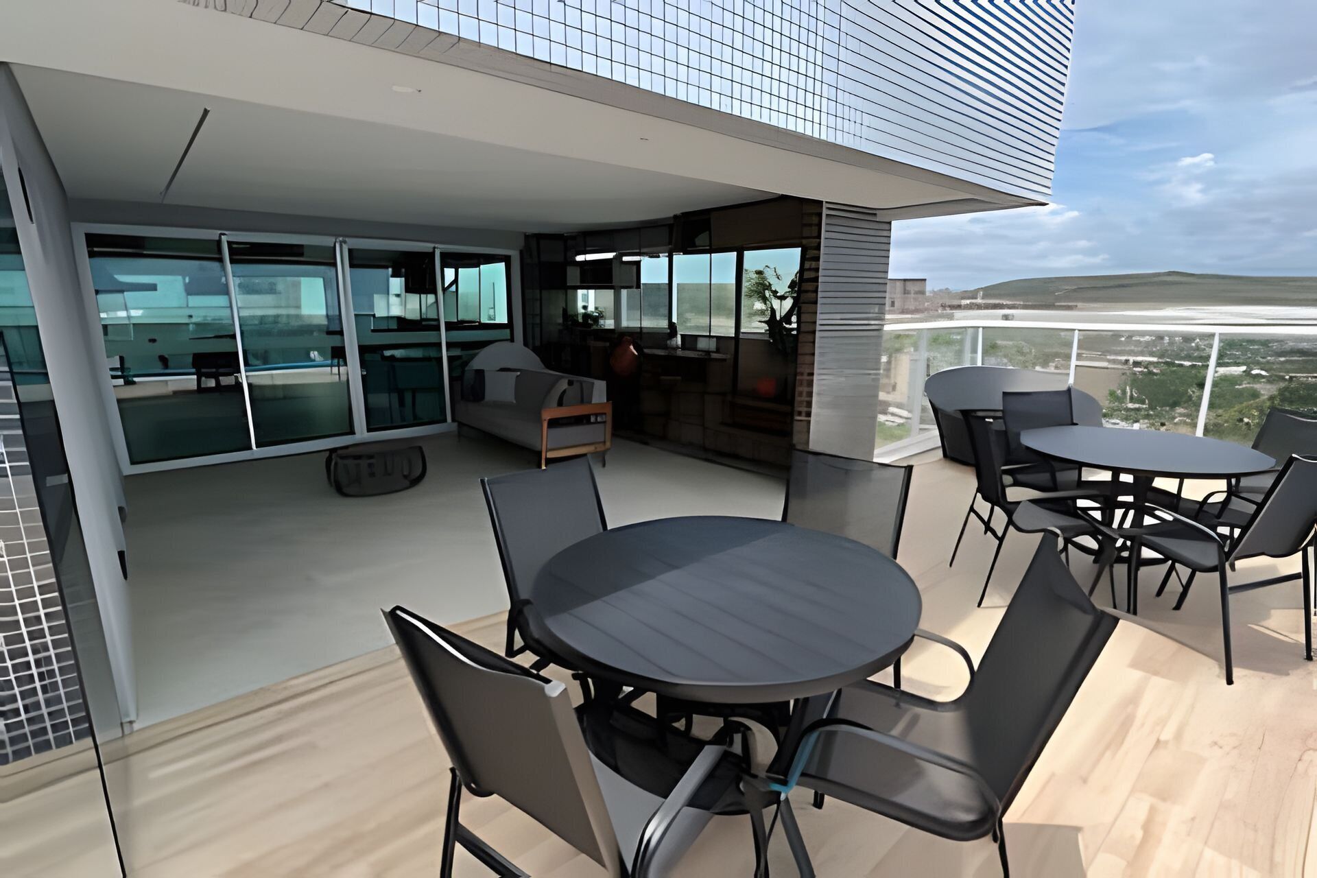 Un'area esterna moderna con zona pranzo, un tavolo rotondo e sedie, un divano e una cucina visibile attraverso porte in vetro.