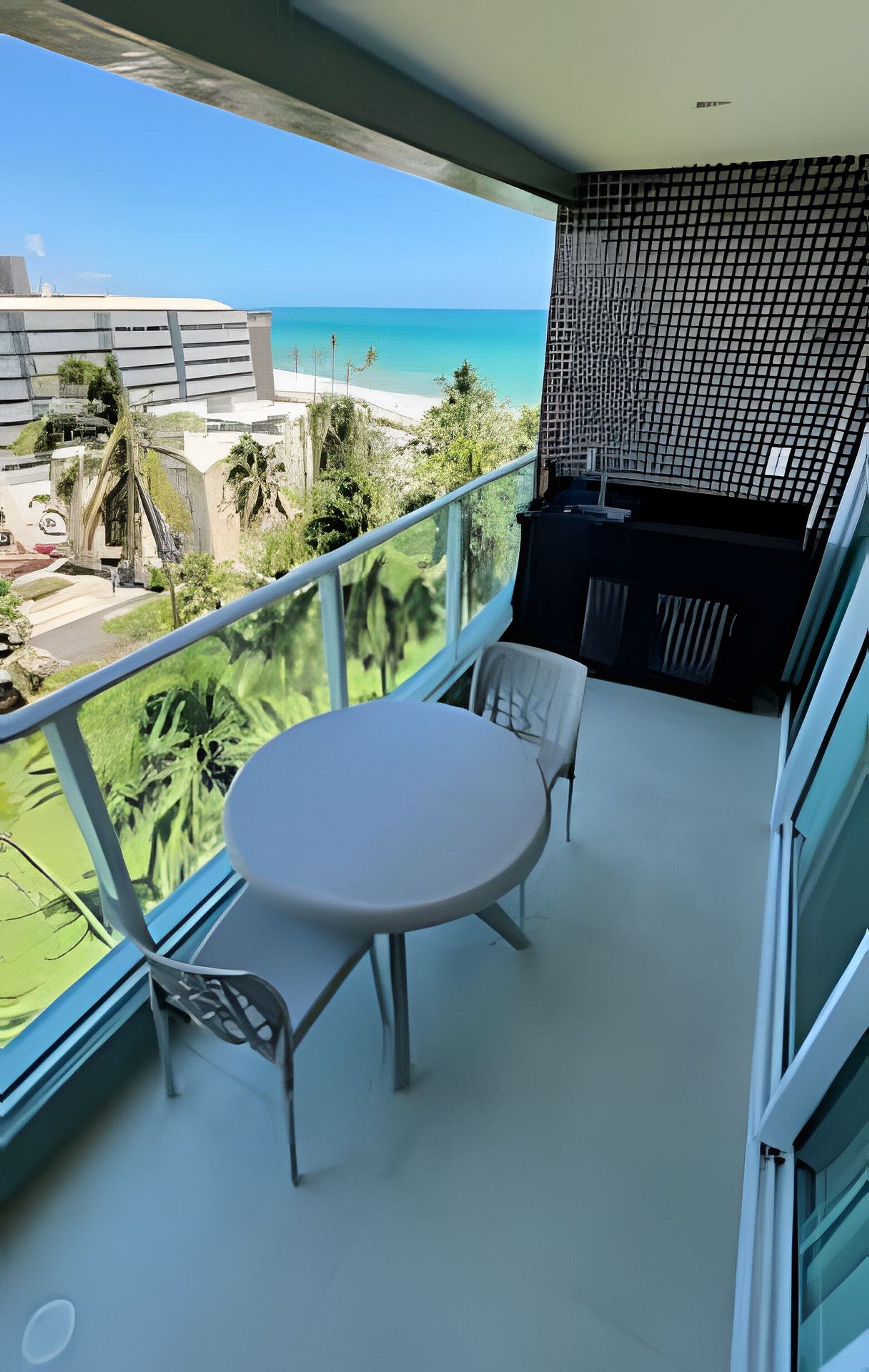 A balcony with a table and chairs, overlooking a beach and ocean.