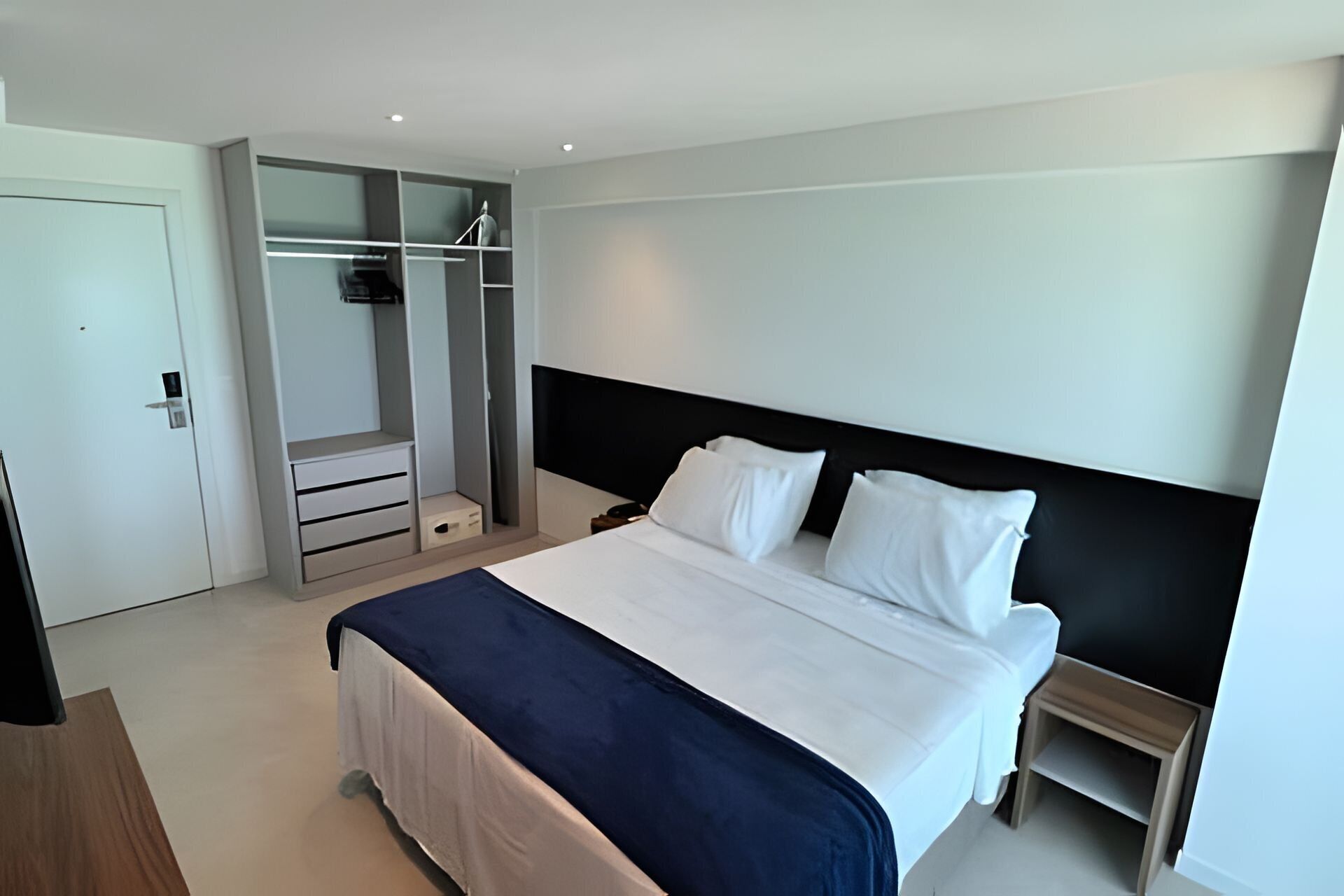 A modern hotel room with a large bed, a walk-in closet, and a small bedside table.
