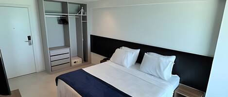 A modern hotel room with a large bed, a walk-in closet, and a small bedside table.