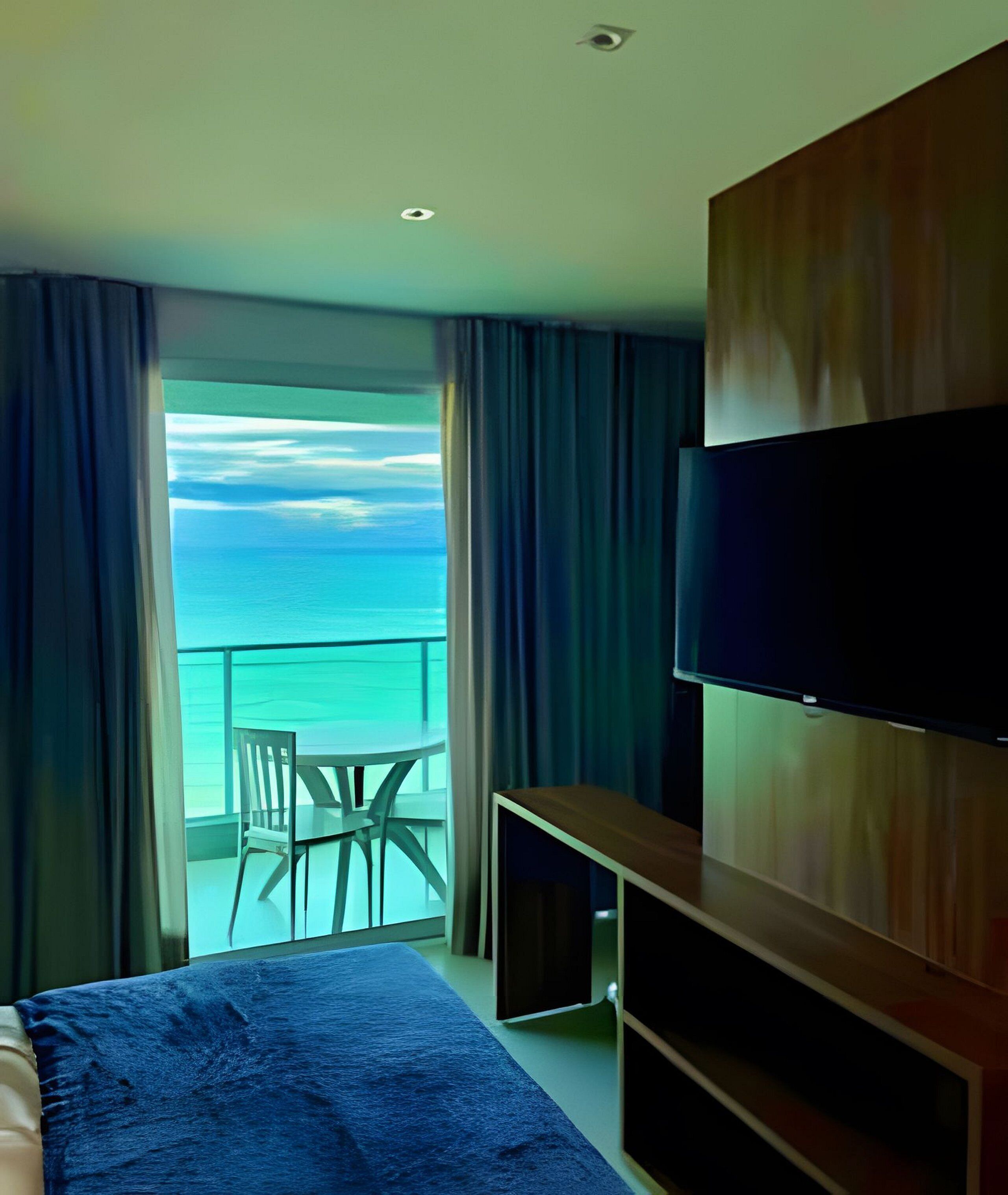A hotel room with a bed, a TV, a desk, and a balcony with a view of the sea.