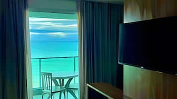 A hotel room with a bed, a TV, a desk, and a balcony with a view of the sea.