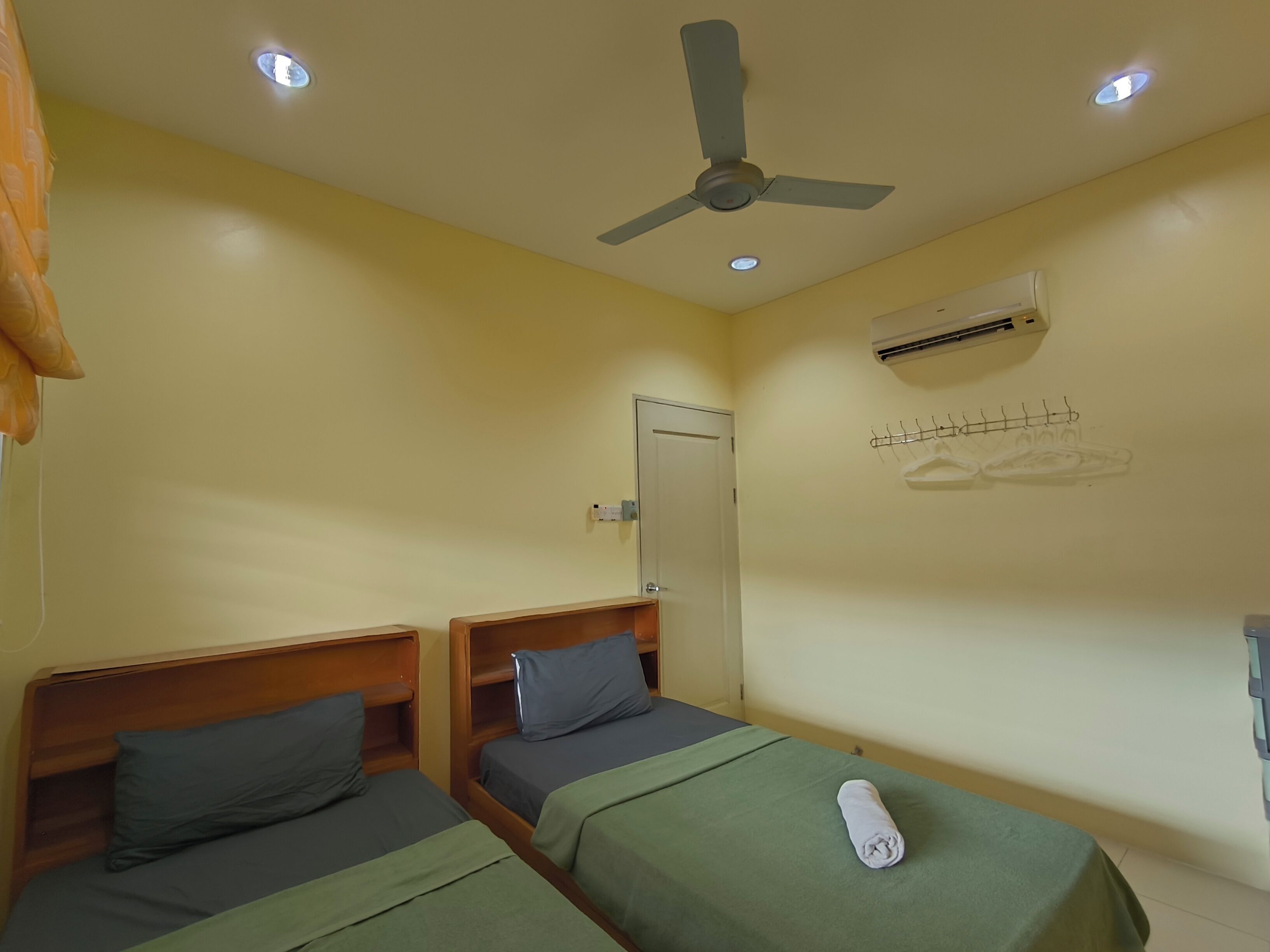 A room with two beds, a ceiling fan, an air conditioning unit, and a towel on one bed.