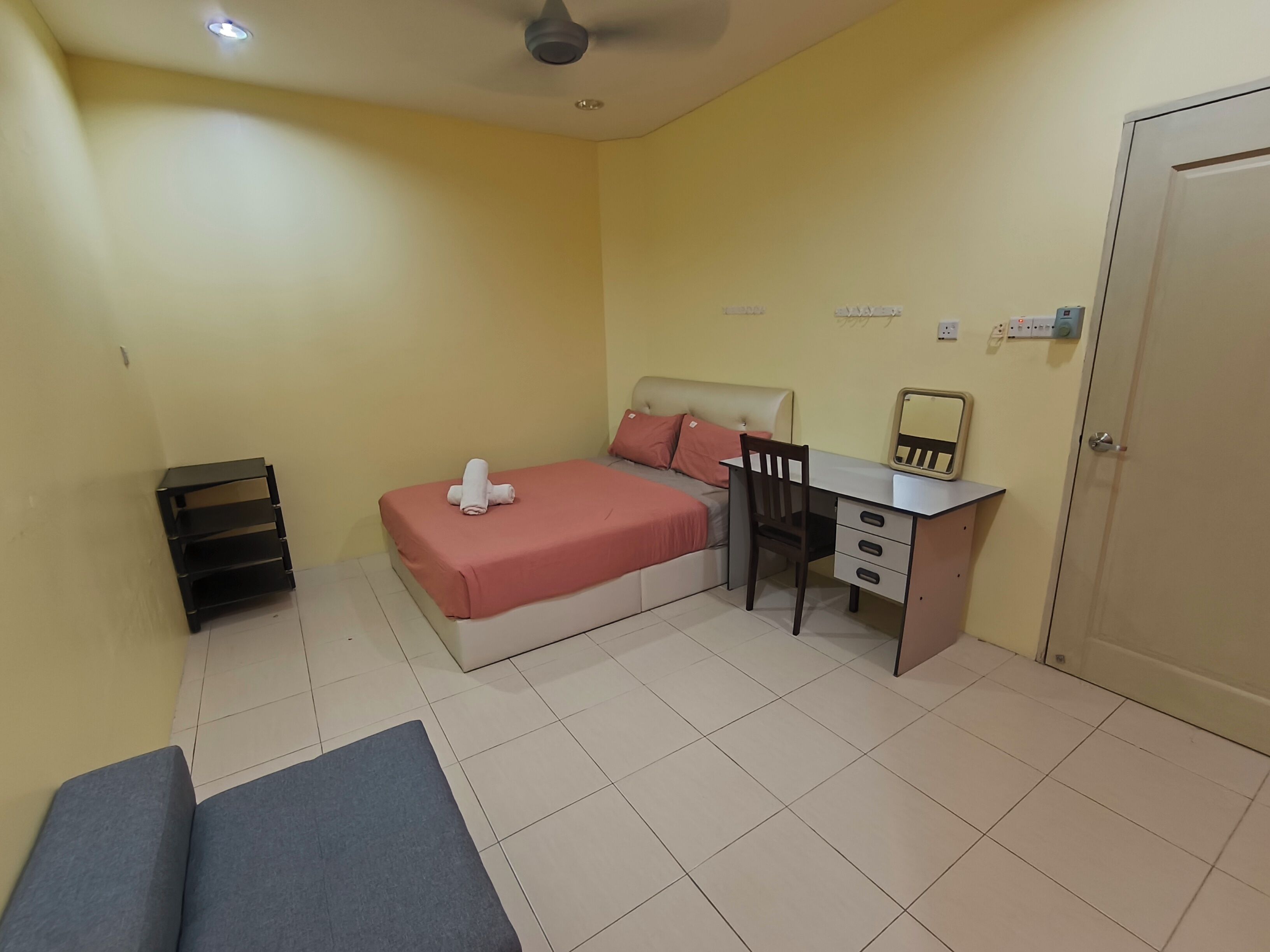 Una habitación pequeña y bien iluminada con cama, escritorio, silla, mesita y puerta.