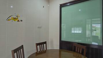 Un salón de conferencias con una mesa redonda, cuatro sillas de madera, paredes de baldosas blancas, una lámpara en el techo y un ventanal con vistas a la vegetación.